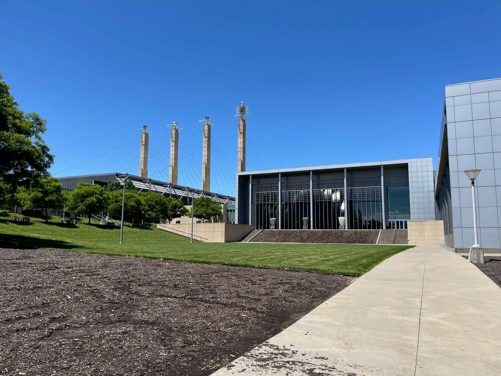 快晴の空の下、Kansas City Convention CenterのGrand Ballroomのガラス張りの建物と、その奥にそびえるBartle Hallの4本のSky Stationsの塔