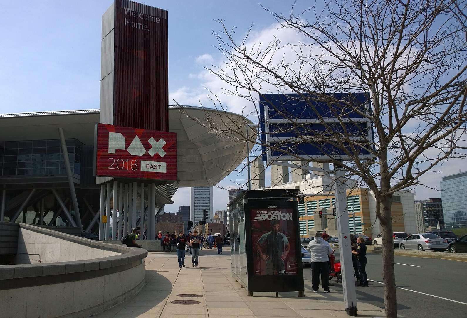 コンベンションセンターの外観。塔状のデジタル看板に「PAX 2016 EAST」と表示され、大きく張り出した曲面屋根が奥へ伸びる。手前は歩道とバス停