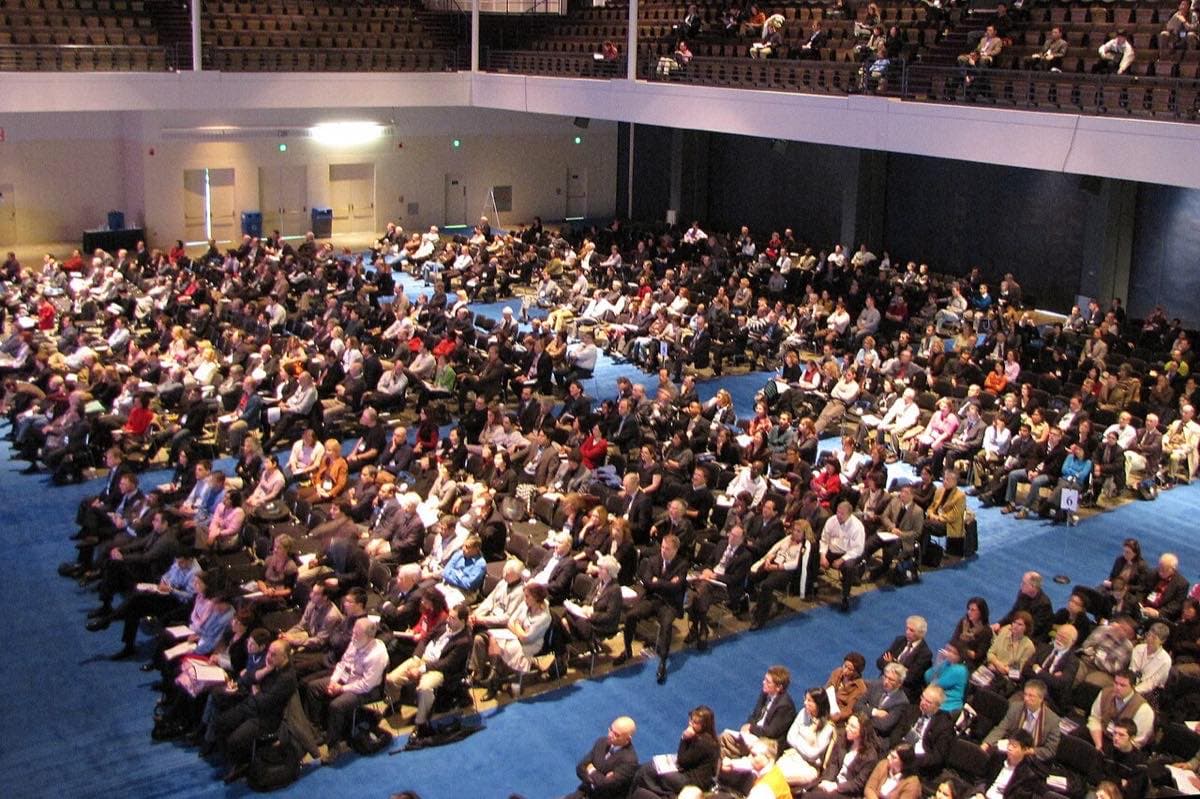 青いカーペットの大ホールに聴衆が満席で座るHynes Convention Centerの講堂