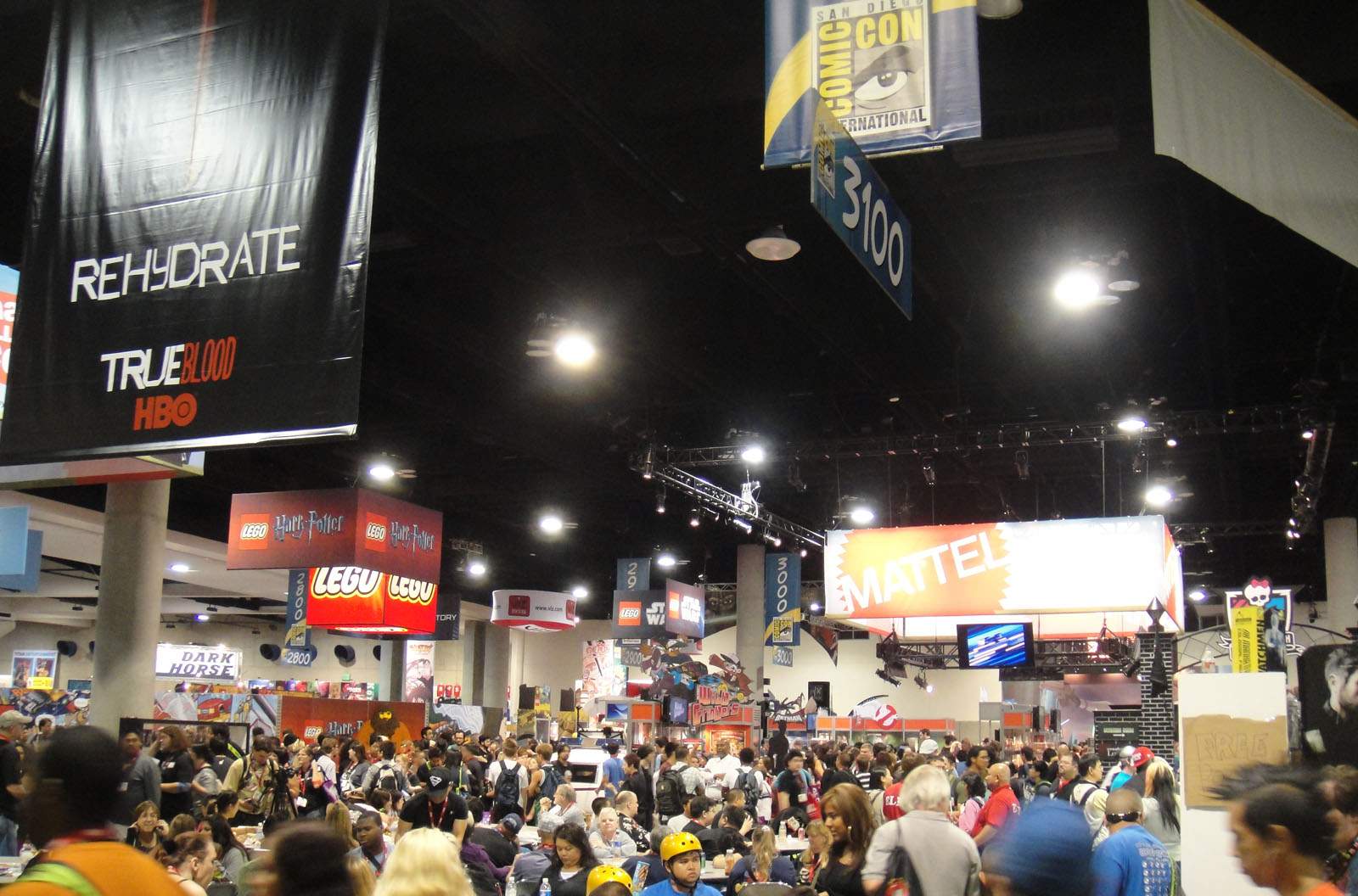 San Diego Comic-Conの展示ホールを見渡した様子。天井からブース番号と各社のバナーが多数下がり、通路は来場者で埋まっている