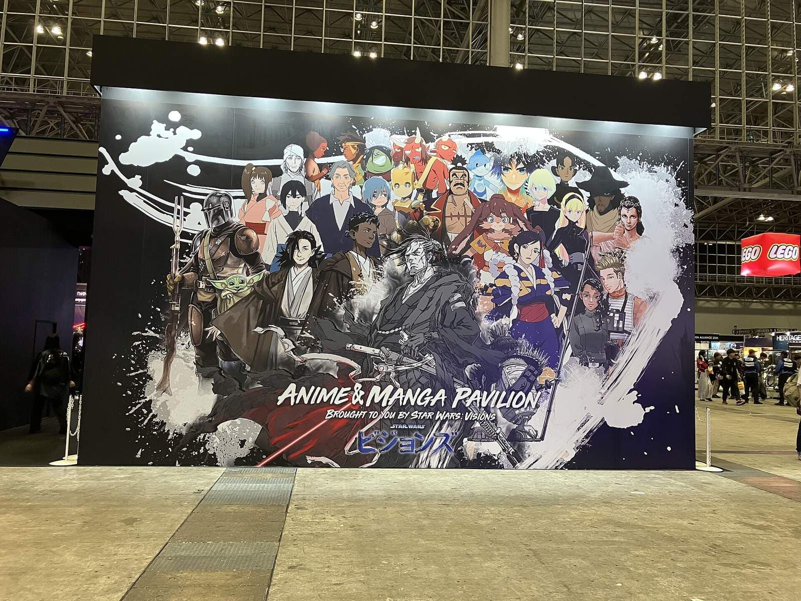 展示ホールに設置された大型の壁面パネル。アニメ調のキャラクターが並んだイラストの下に「ANIME & MANGA PAVILION」の文字があり、右奥にレゴの看板が見える