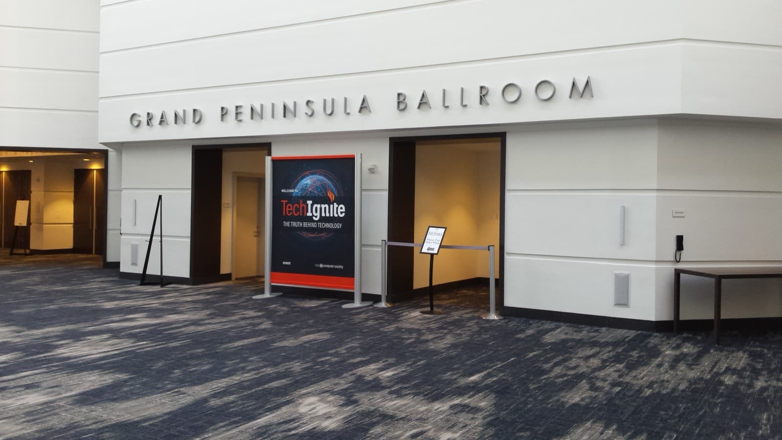 ホテルの宴会場の入口。壁の上部にGrand Peninsula Ballroomの立体文字があり、入口の前にカンファレンスの案内パネルが立っています