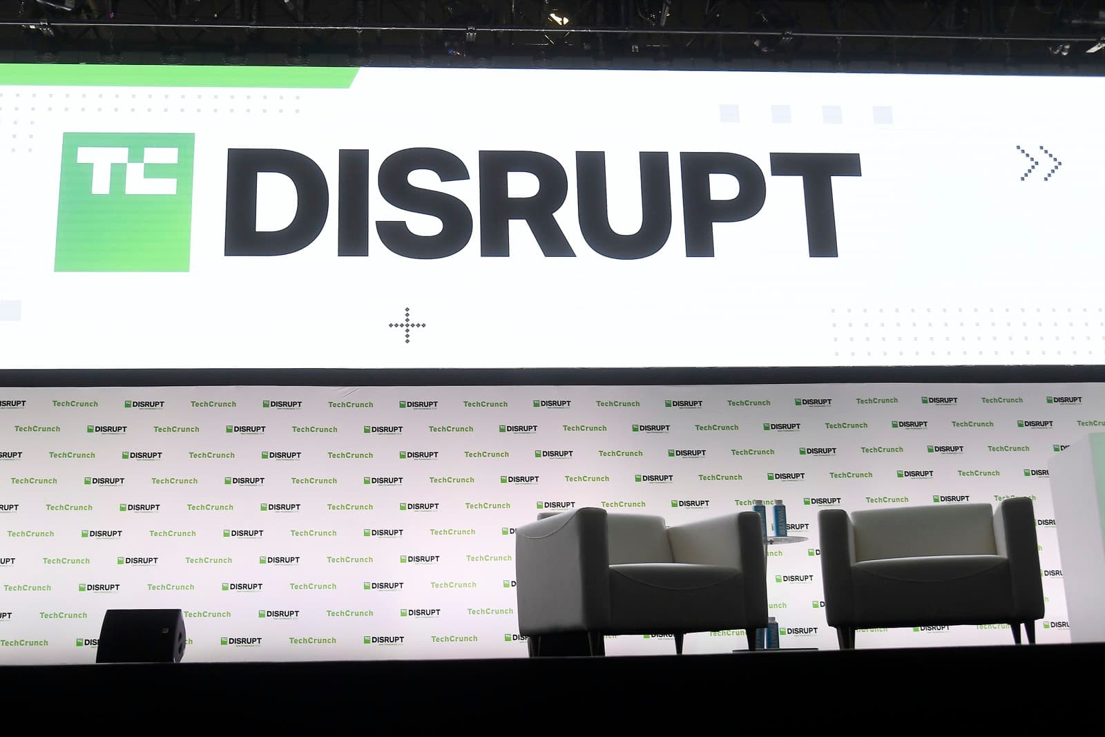 TechCrunch DisruptのメインステージLEDウォール。DISRUPTのロゴの下に登壇者用の白い椅子が2脚並んでいる
