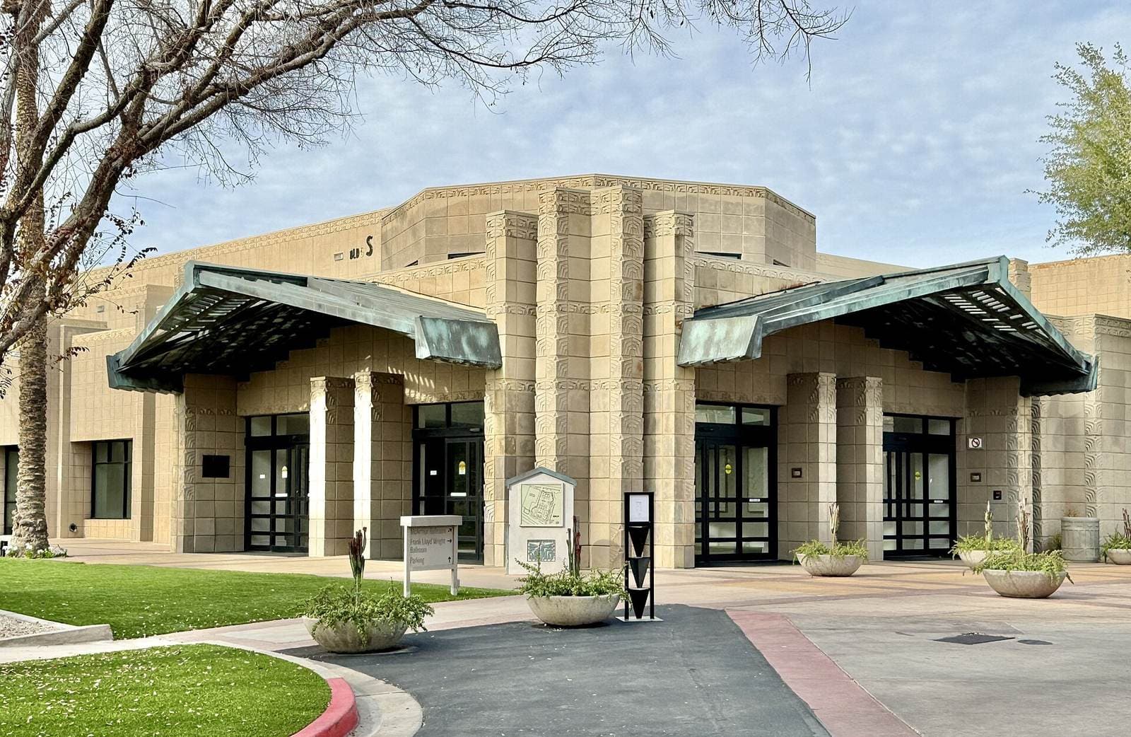 Arizona Biltmoreの会議棟の入口。銅葺きの庇が左右に張り出し、その下に自動ドアが並ぶ。手前の芝生の脇に館内案内板が立っている