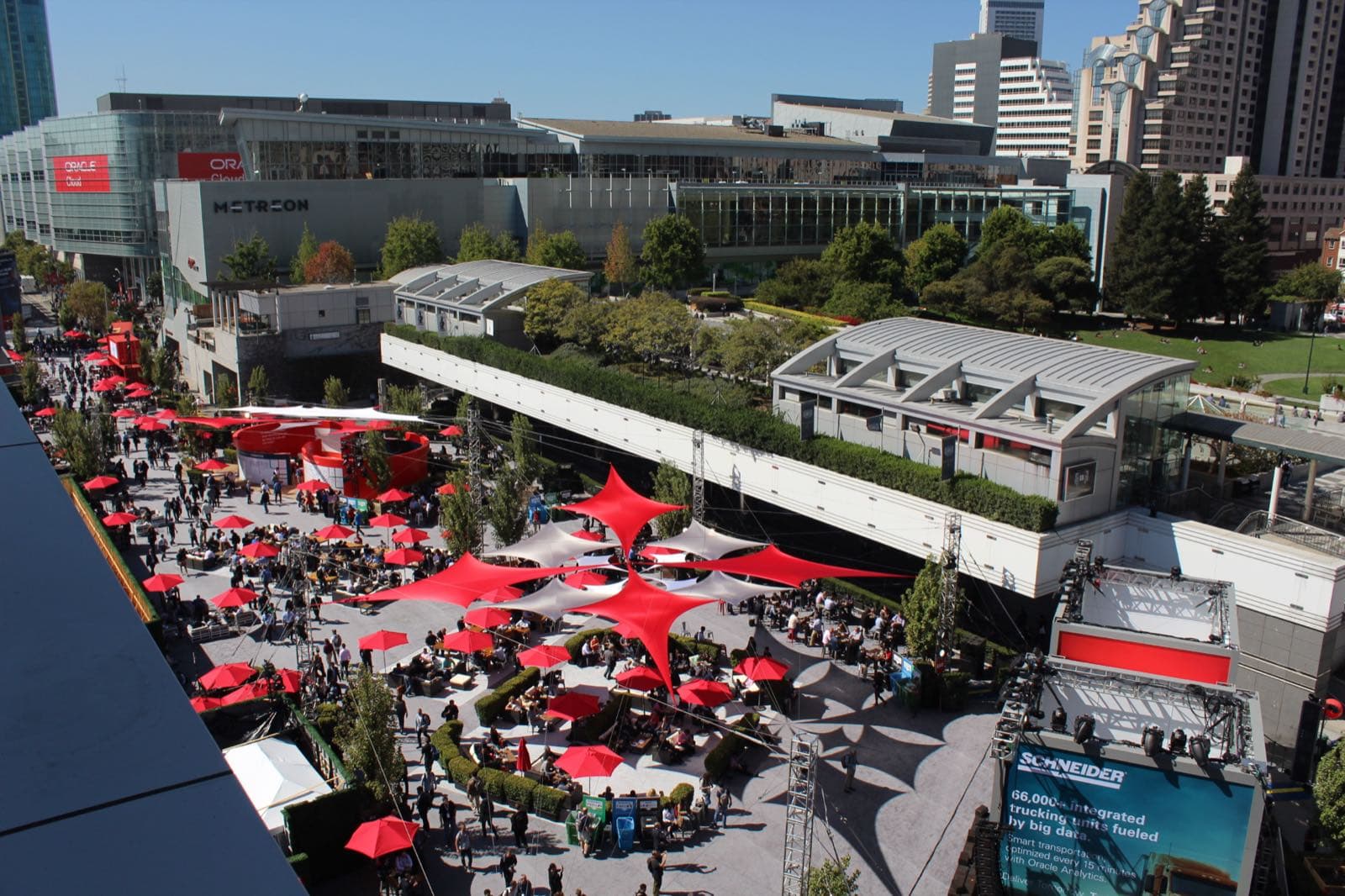 高層階から見下ろしたYerba Buena Gardensの広場。赤い日よけとパラソルが並び、来場者が屋外の席に集まっている。奥にMETREONの建物とサンフランシスコ中心部の高層ビル群が見える