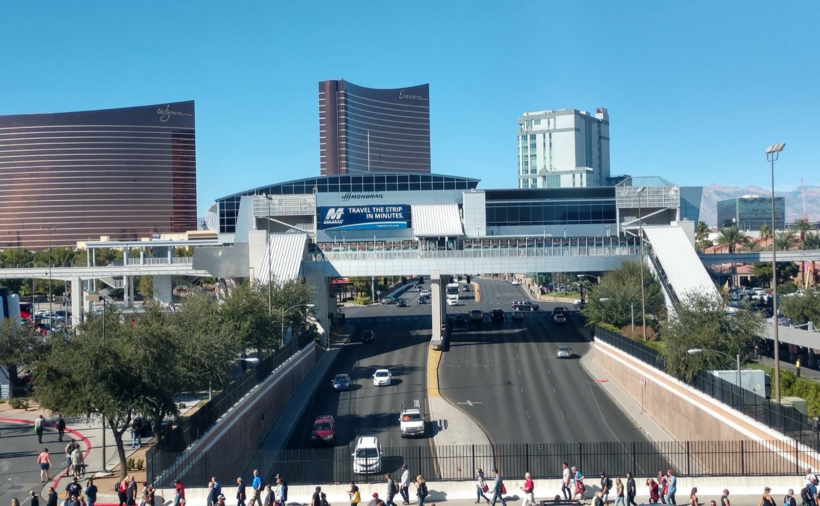 高架のモノレール駅と、その手前を横切る歩行者用の連絡橋。下を幹線道路が通り、奥にラスベガスの高層ホテルが並ぶ