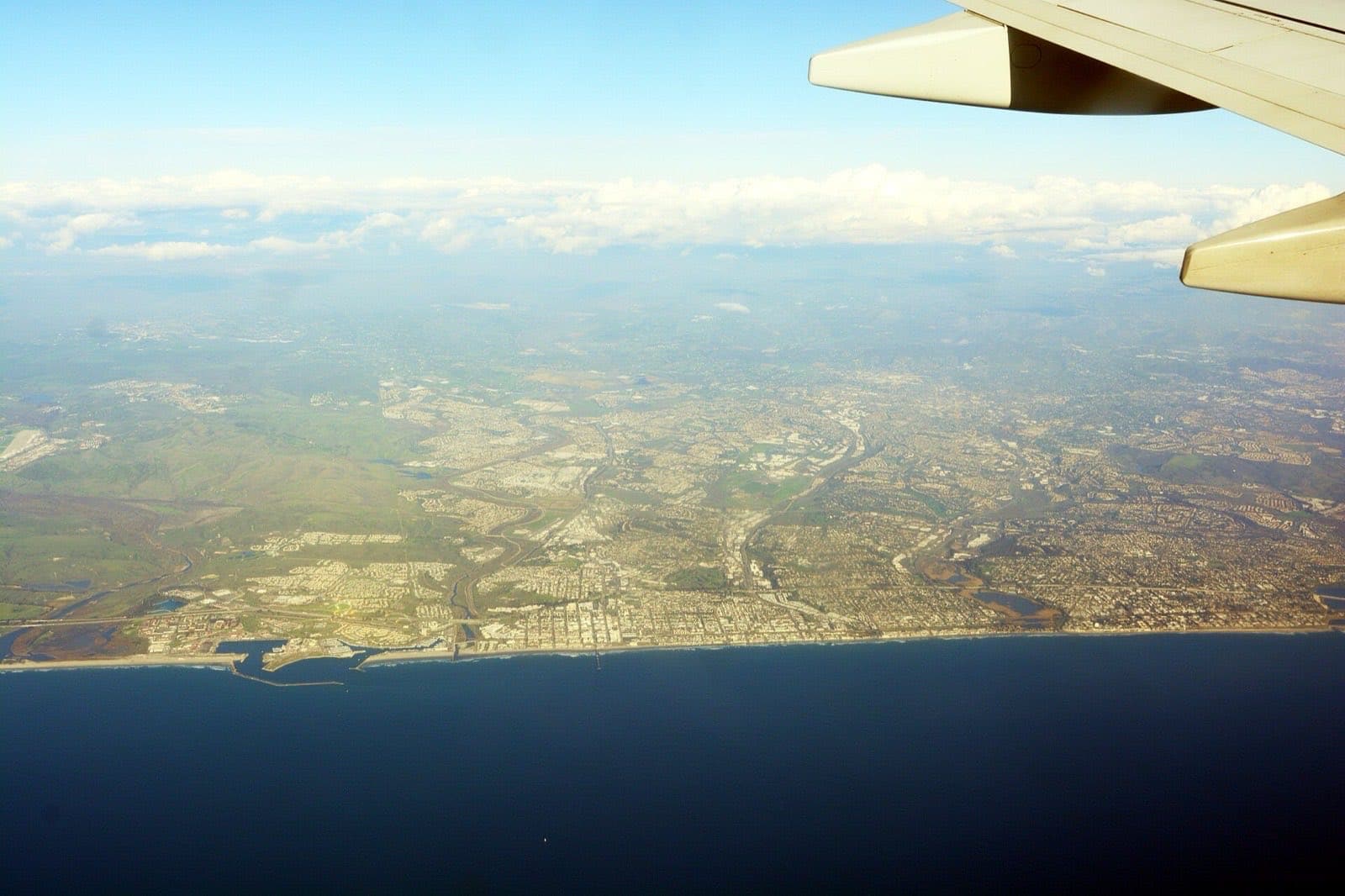 旅客機の窓から見下ろした南カリフォルニア沿岸。海岸線に沿って低層の市街地が広がり、高層ビル群は見当たらない