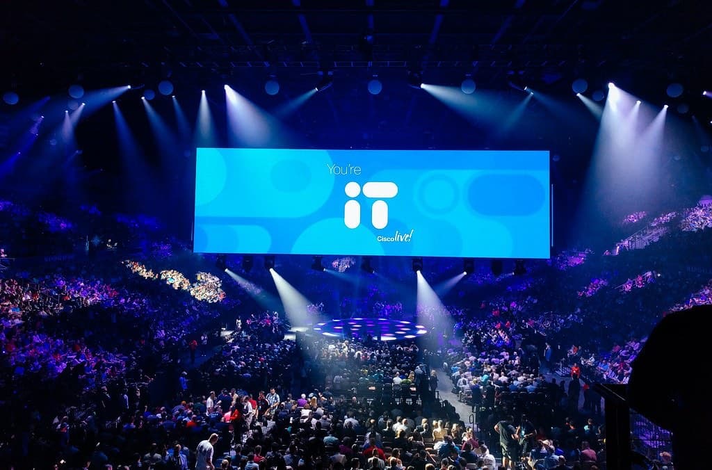 青と紫の照明に照らされたアリーナの基調講演会場。中央の巨大スクリーンにCisco liveのロゴが映り、すり鉢状の客席が参加者で埋まっている