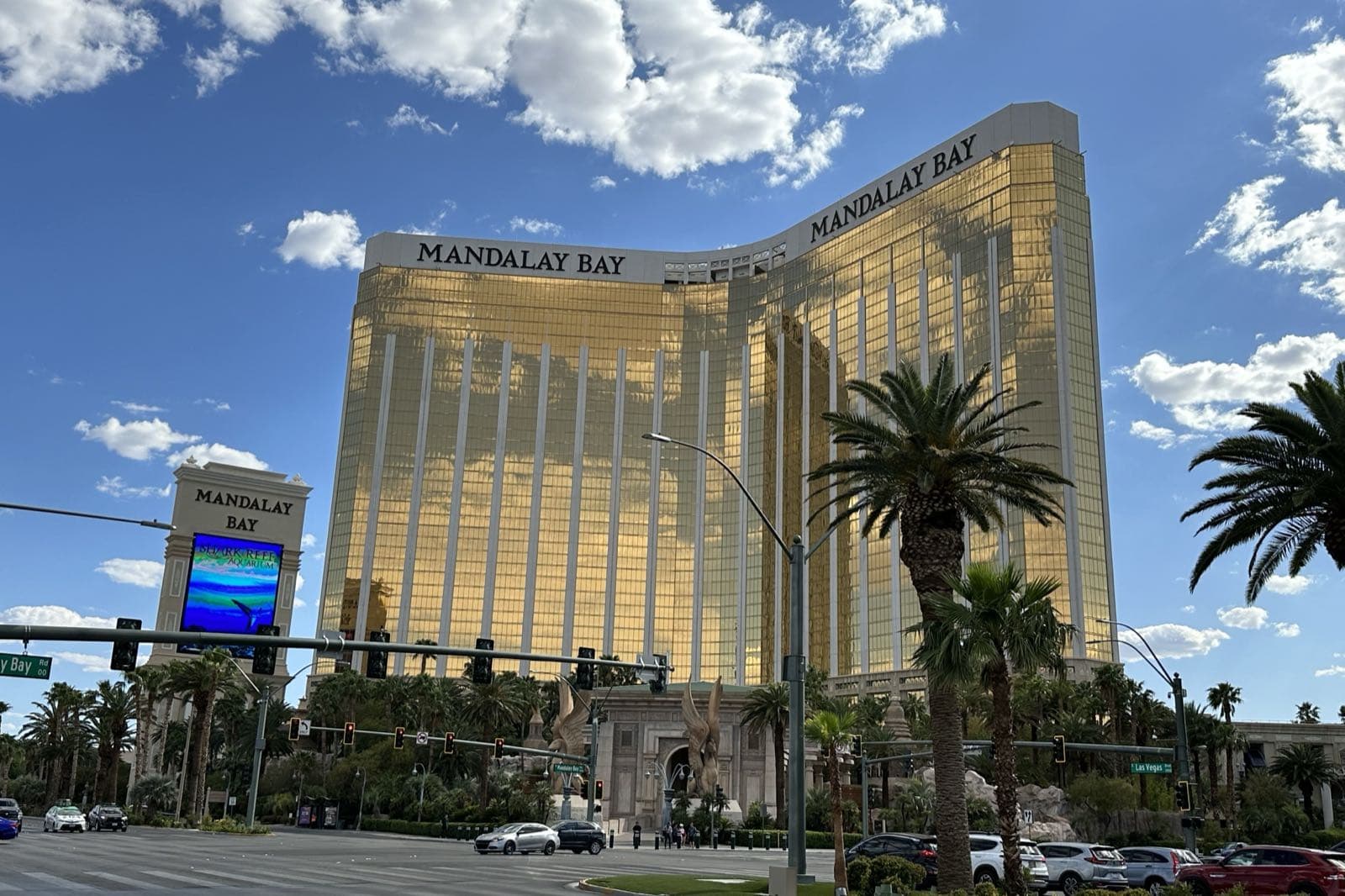 青空の下、ラスベガス大通りの交差点越しに見える金色のMandalay Bayの2棟のタワーとヤシの木