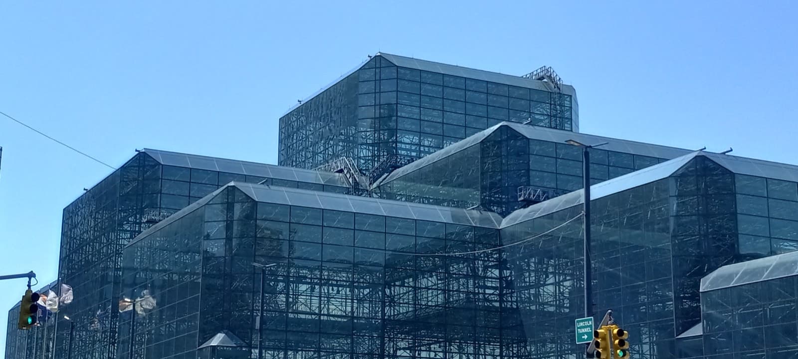 ガラスの箱を段状に積み重ねたJavits Center本館の外観を、11番街側の交差点から見上げた様子。手前に信号機と「LINCOLN TUNNEL」の道路標識が写っています