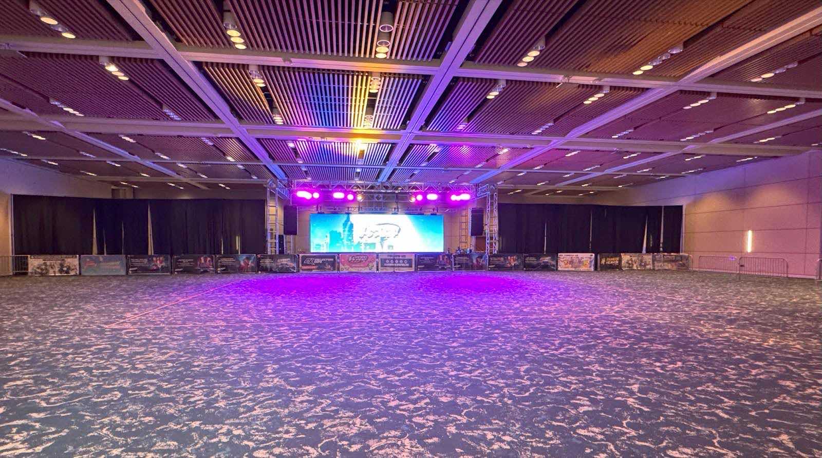 Santa Clara Convention Centerのボールルーム内部。木格子の天井の下に無人のカーペット床が広がり、奥にLEDスクリーンを備えた仮設ステージがある