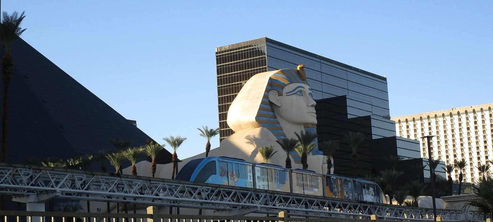 高架の軌道を走る無料トラムの車両。背後にLuxorのピラミッドとスフィンクス像、その奥に高層ホテルが見える