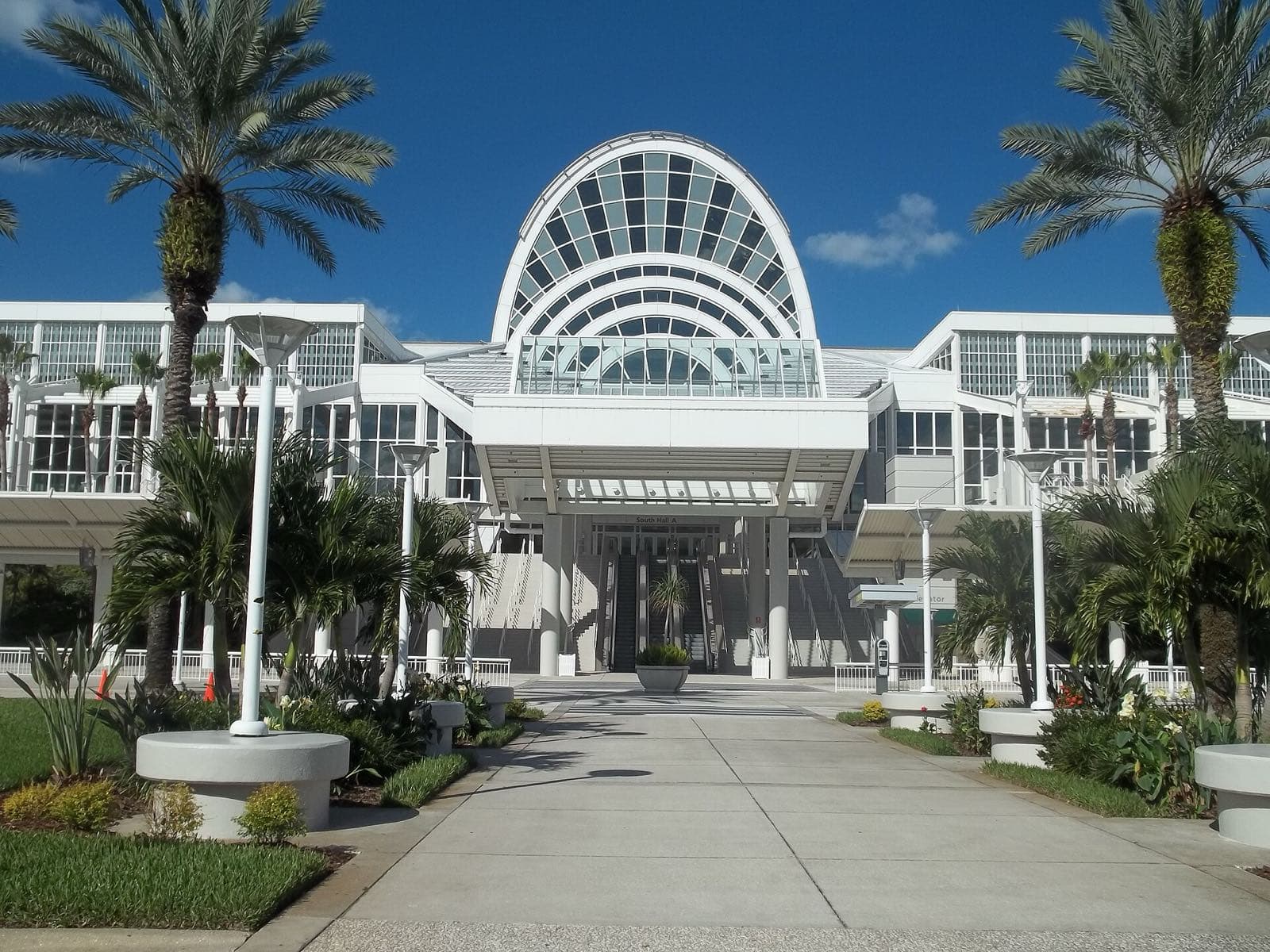 Orange County Convention CenterのSouth Hall A入口。ヤシの木が並ぶ遊歩道の先に、庇の下のエスカレーターとSouth Hall Aの表示が見える