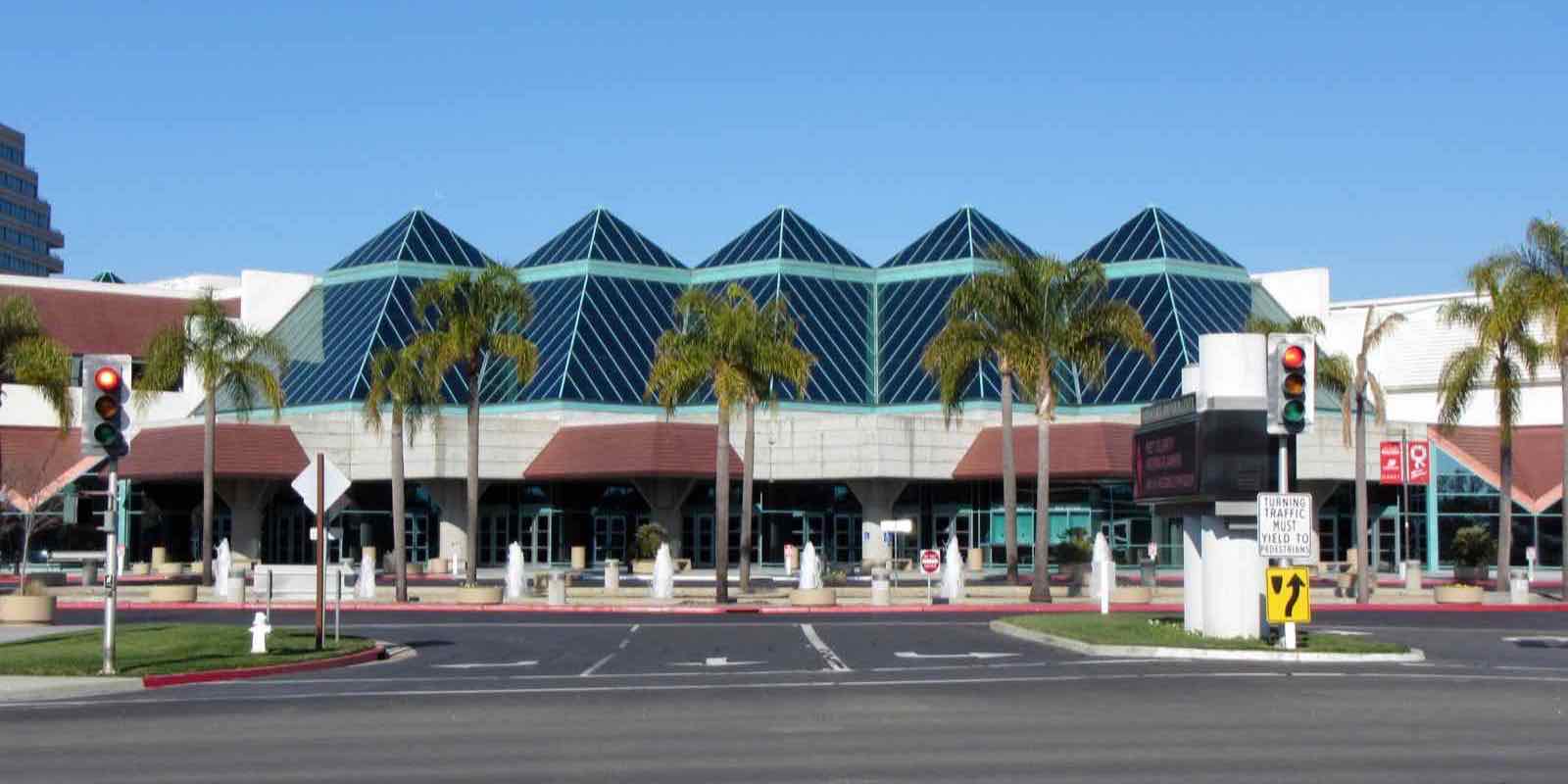 ヤシの木と噴水が並ぶ通りに面した、青緑色のピラミッド型ガラス屋根が連なるSanta Clara Convention Centerの正面外観