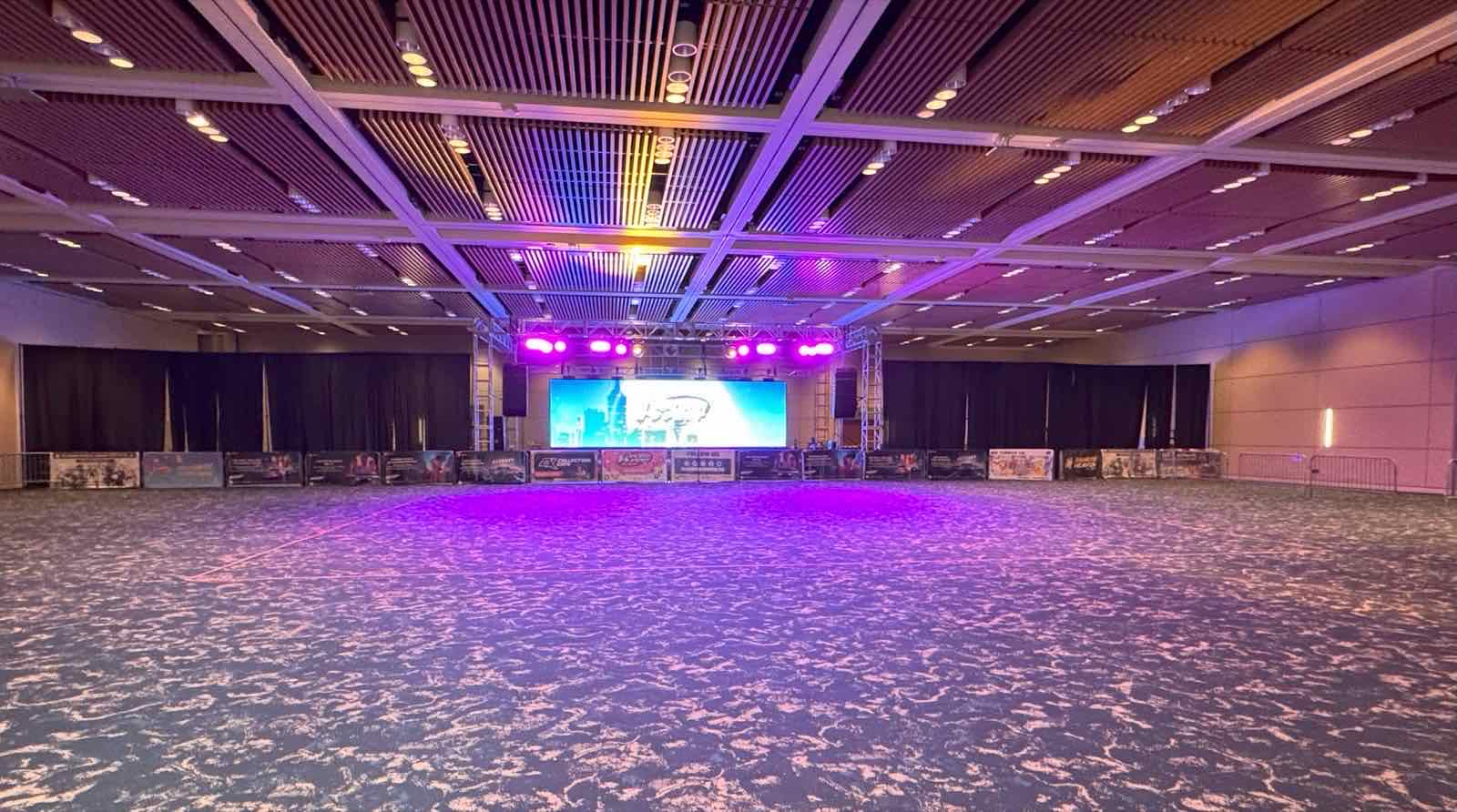 格子状の天井と照明トラスの下に舞台が組まれた、Santa Clara Convention Centerの展示ホール内部